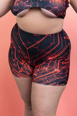 Freedom Rave Wear red and black circuit-pattern shorts, focused on fit and design, model's back to camera against a soft pink background