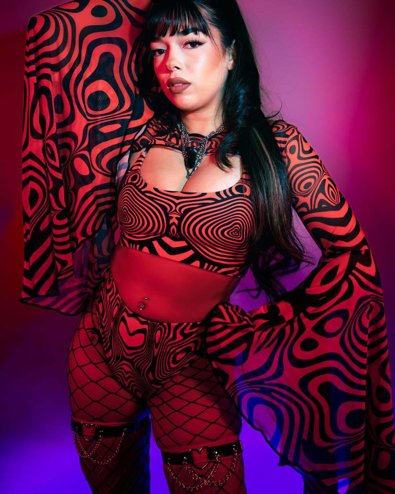 Model in psychedelic red and black outfit with bell sleeves, perfect for rave outfits, posed under colorful lighting.