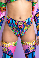An up close photo of a girl wearing rave bottoms that resemble high waisted bikini bottoms. They are printed with a rainbow stained glass design.