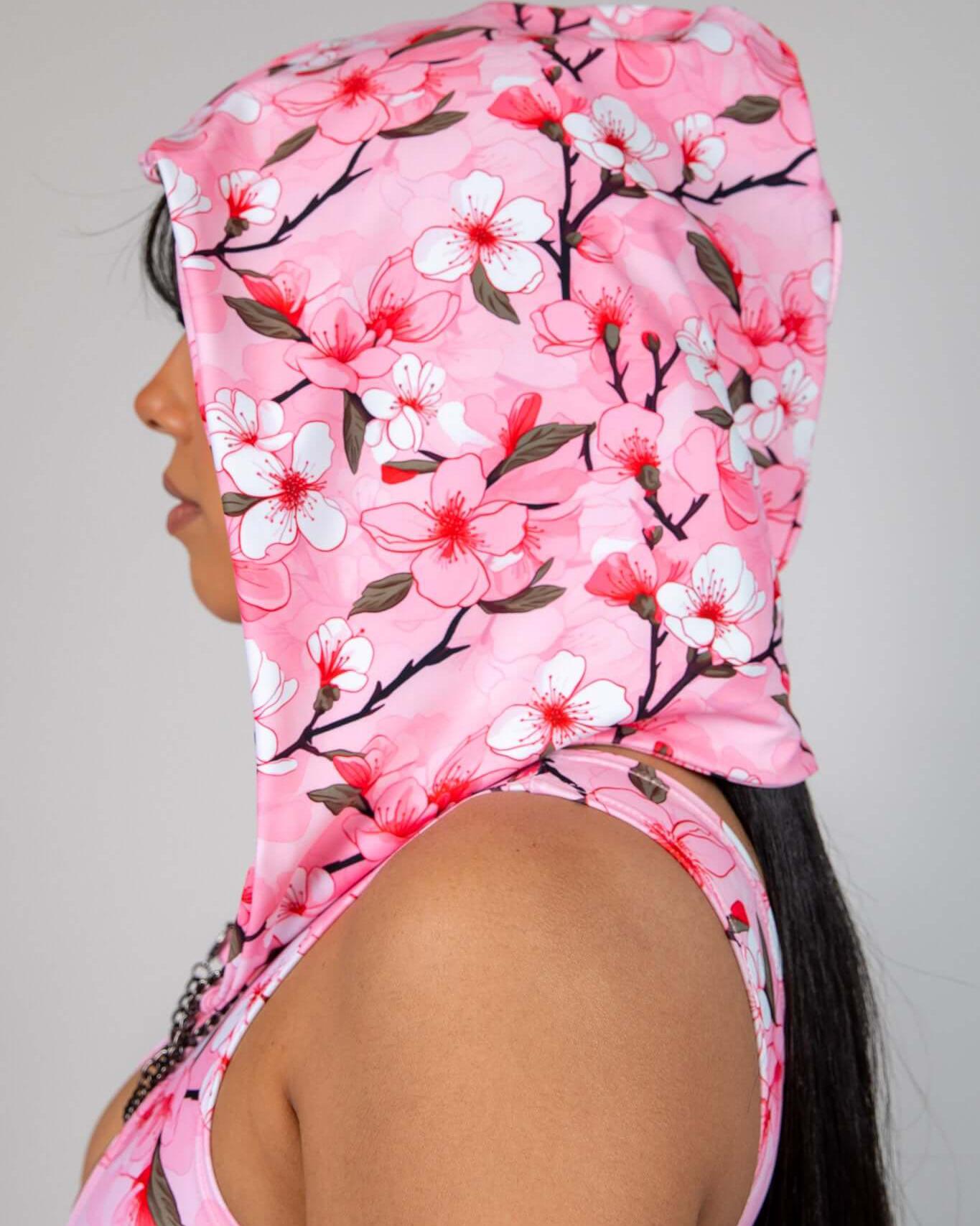 Side view of a woman wearing a Sakura Assassin Hood with pink cherry blossom design, perfect for rave outfits.