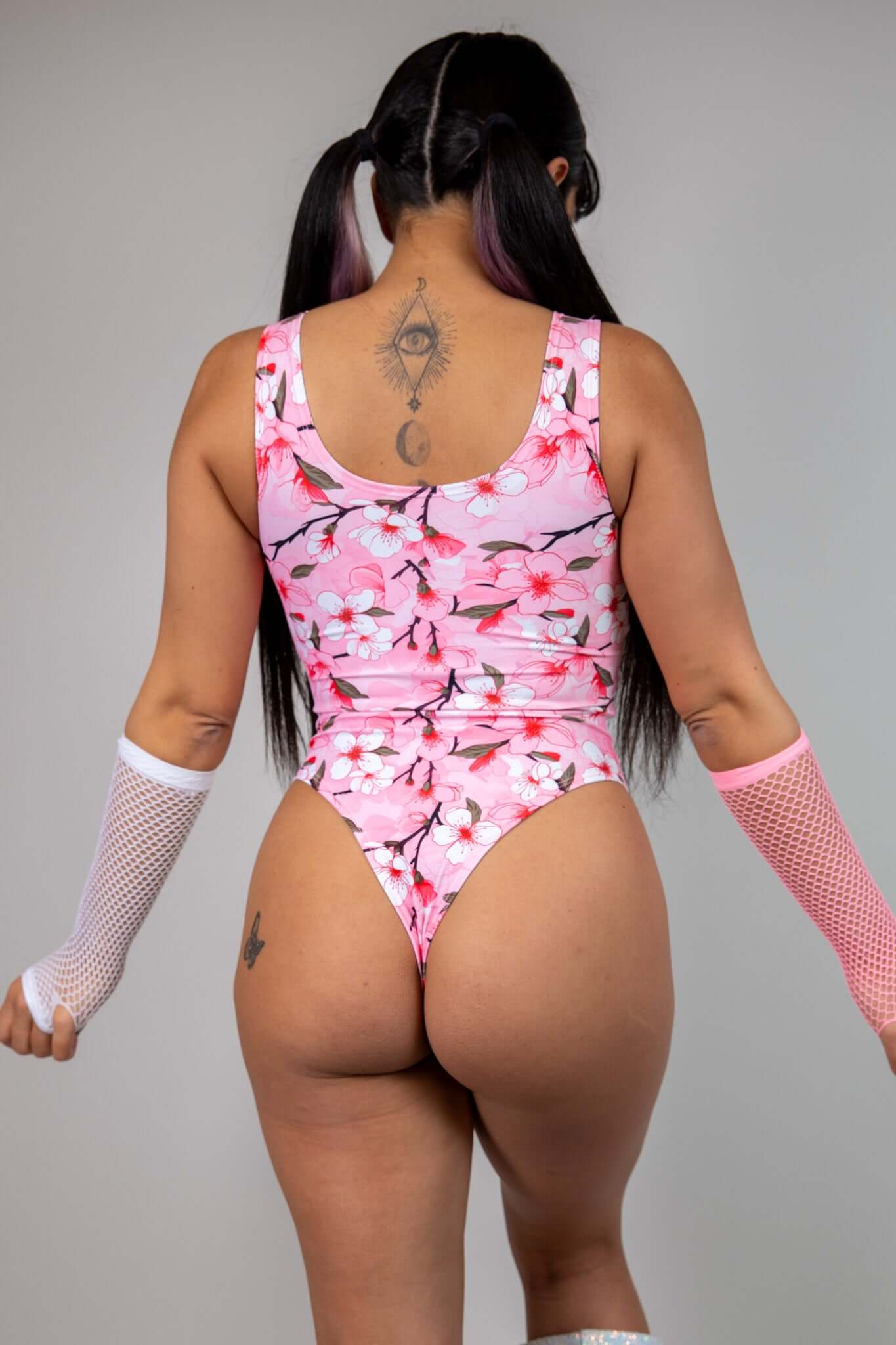 Back view of pink keyhole bodysuit with white and pink cherry blossom print, featuring cheeky fit, perfect for rave and festival looks.