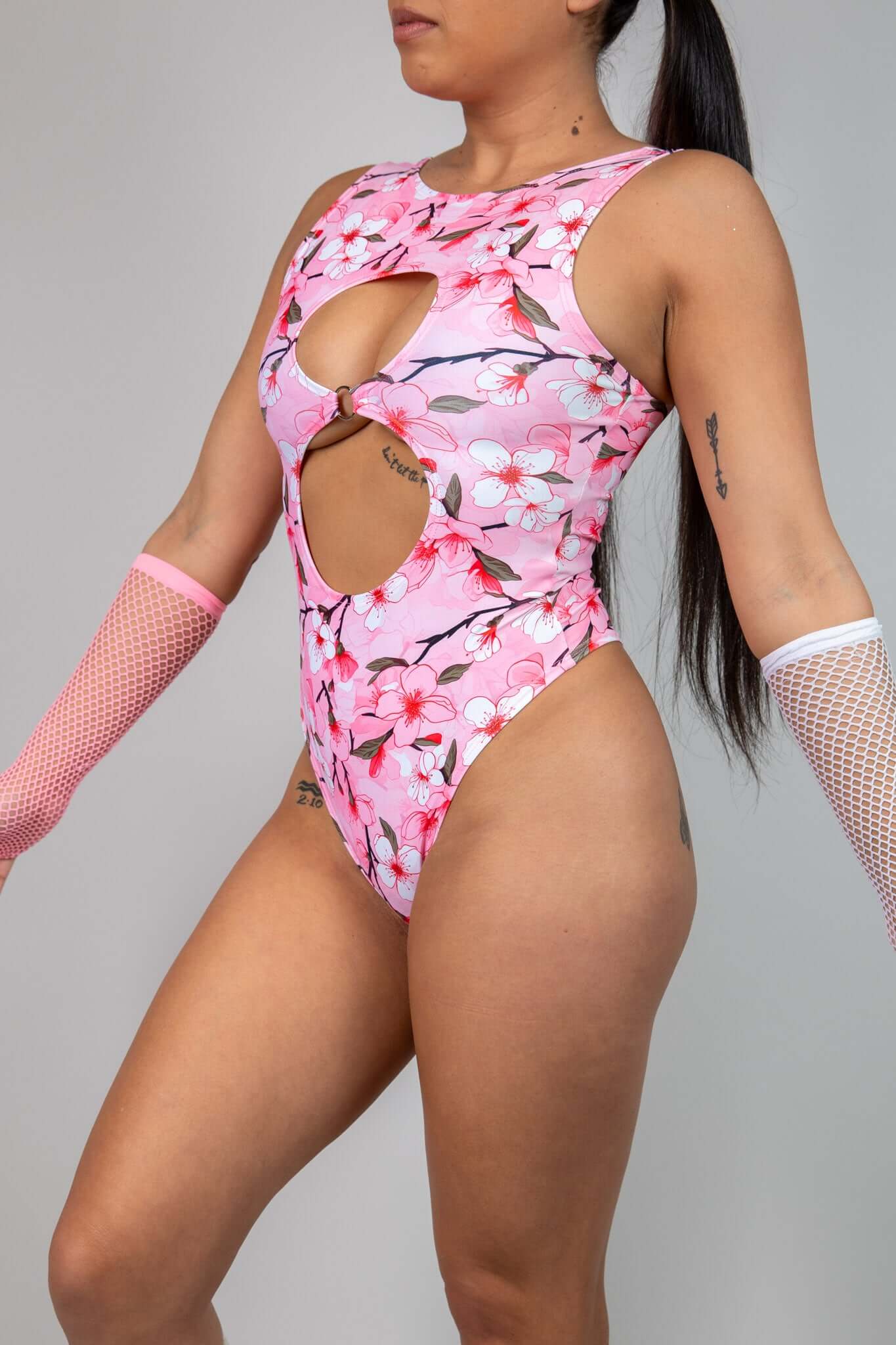 Side view of pink keyhole bodysuit with white and pink cherry blossom print, showcasing cutout details, perfect for rave fashion.