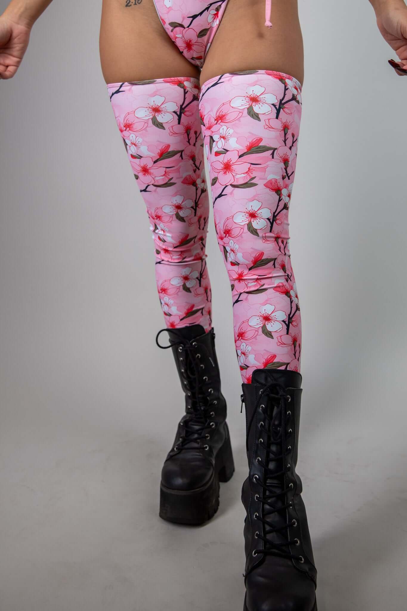 Close-up of pink leg sleeves with white and pink cherry blossom print, styled with black platform boots, perfect for rave and festival outfits.