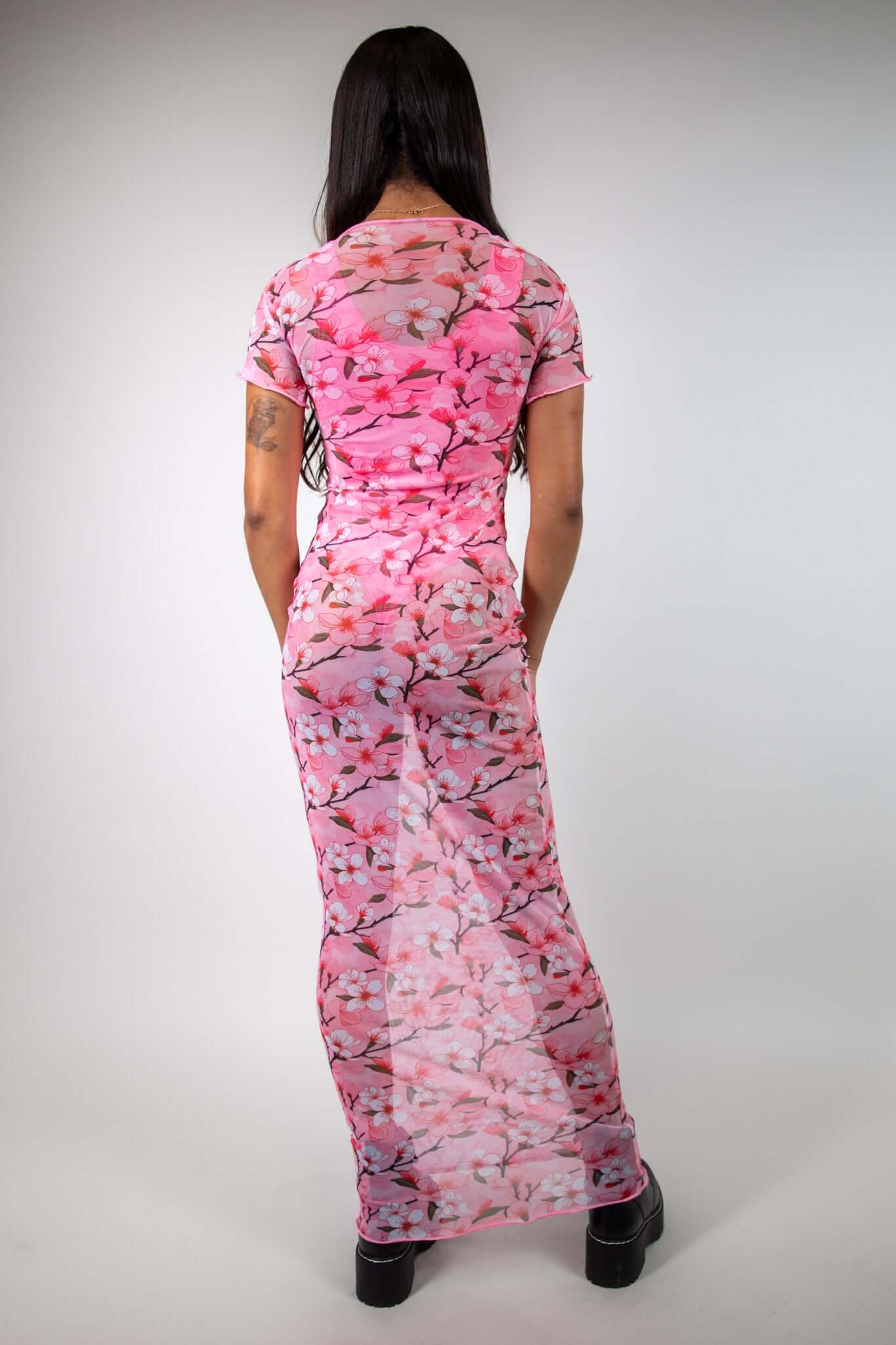 Back view of pink mesh maxi dress with baby tee design and white and pink cherry blossom print, styled with black boots, perfect for festivals.