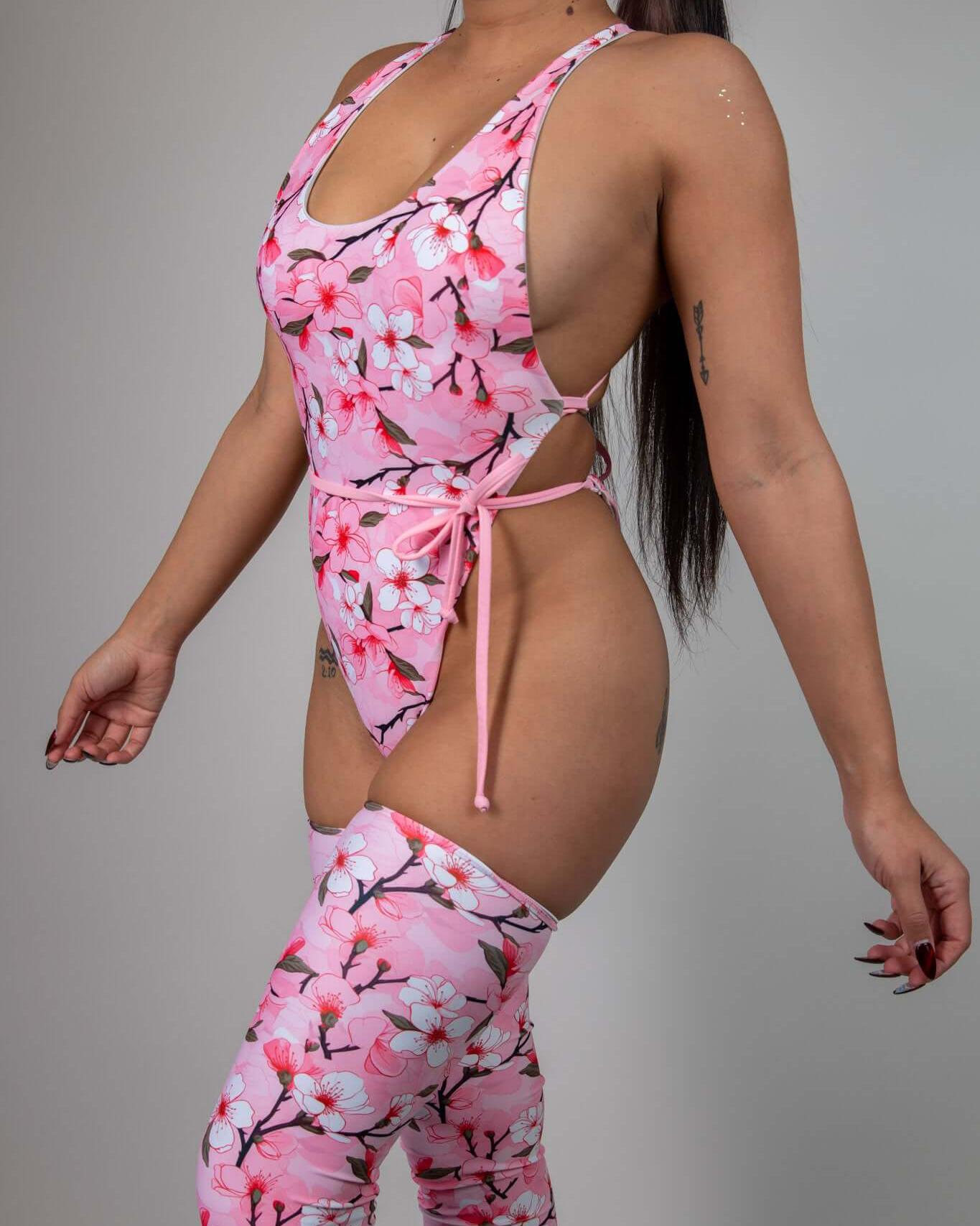 Woman in vibrant pink cherry blossom themed one piece swimsuit, showcasing a cheeky design perfect for rave outfits.