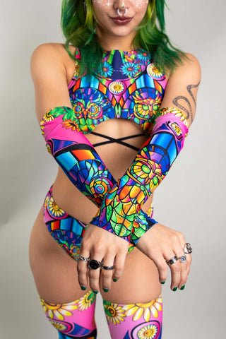 An up close photo of a girl with green hair wearing rainbow stained glass inspired arm sleeves and a matching bikini set.
