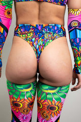 An up close photo of a girl wearing rave bottoms that resemble high waisted bikini bottoms. They are printed with a rainbow stained glass design. She is facing away from the camera.
