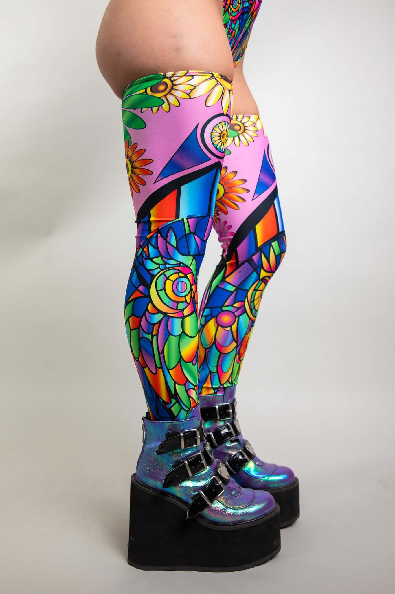 An up close photo of a girl's legs. She is wearing rainbow stained glass printed leg sleeves that go up to her mid thigh.