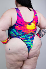 Colorful back view of aplus-size model in a vibrant sunset-themed swimsuit, showcasing bold patterns and style.