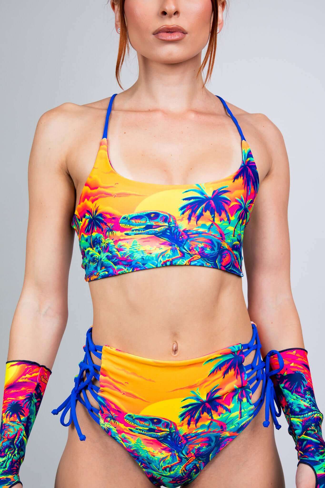 Freedom Rave Wear two-piece set featuring a neon dinosaur sunset print. Bralette top and high-waisted shorts with lace-up sides for a bold rave look.