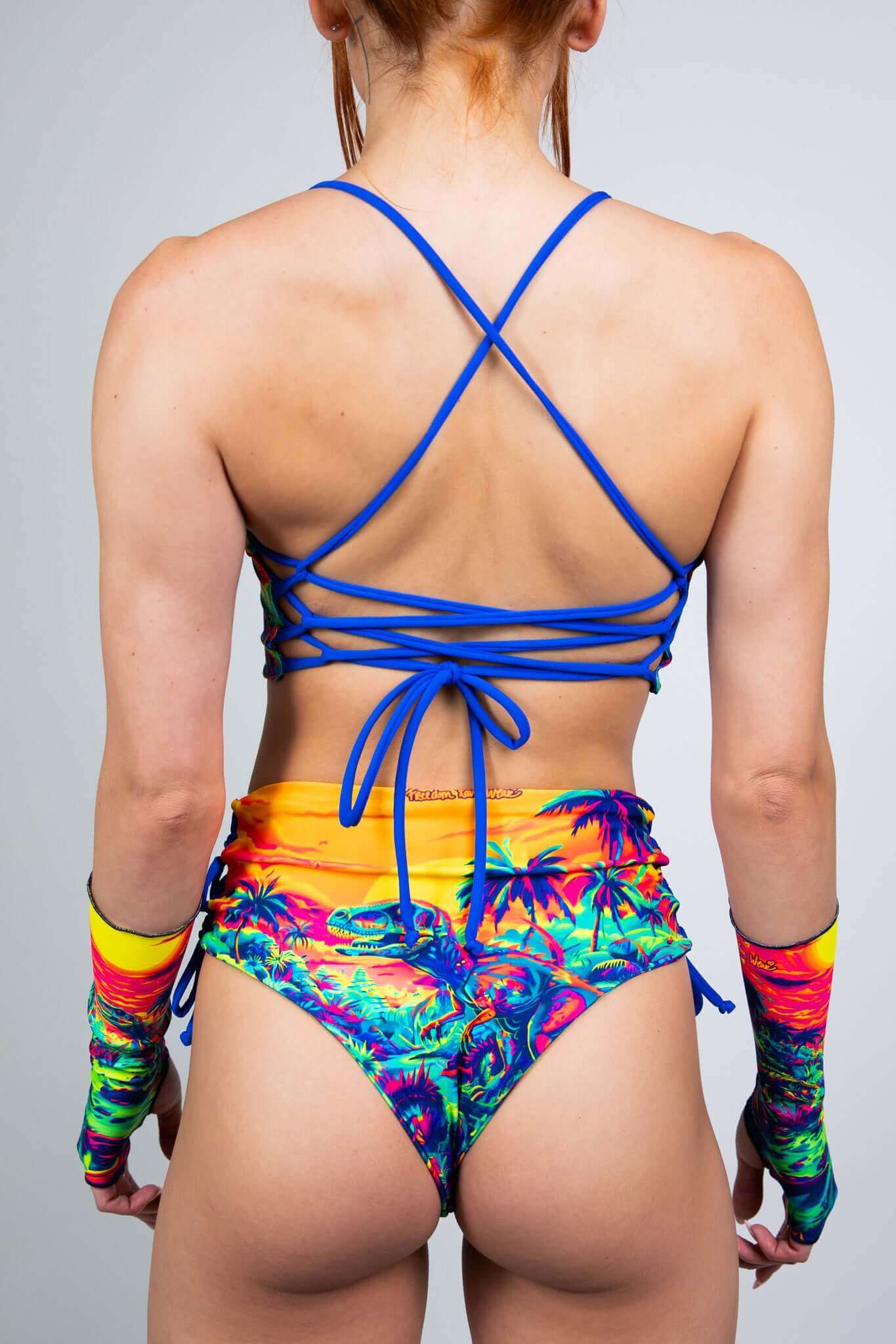 Freedom Rave Wear neon dinosaur sunset print bralette and high-waisted shorts with blue criss-cross back and lace-up sides. Vibrant and edgy for rave vibes.