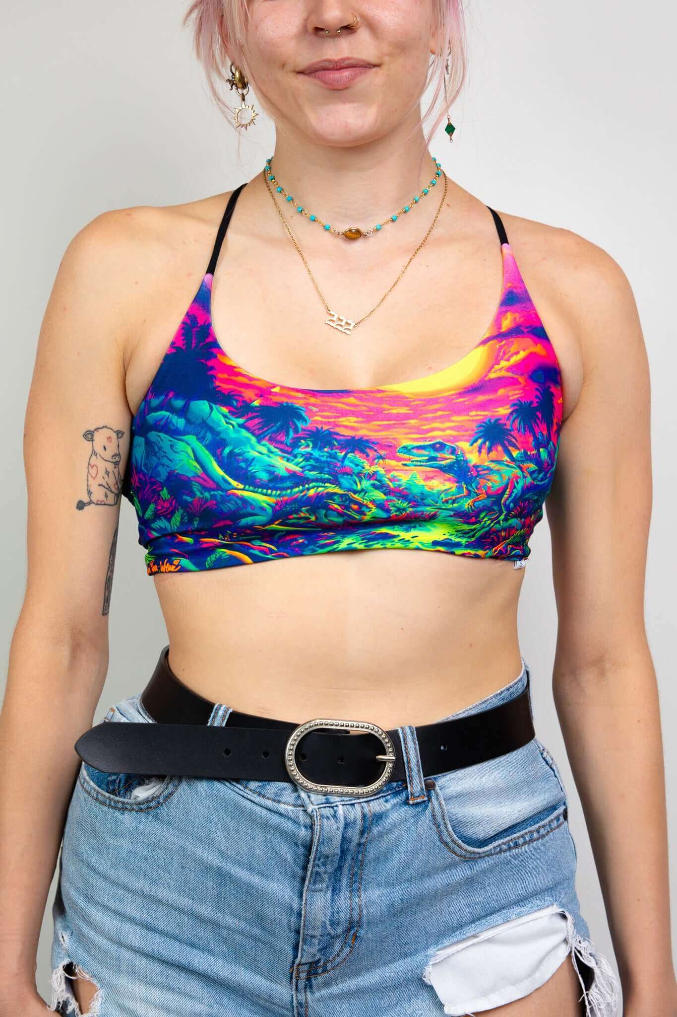 Freedom Rave Wear crop top with a vibrant dinosaur print, paired with ripped denim shorts and a black belt, perfect for rave festivals.