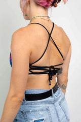 Side view of a woman in a Freedom Rave Wear top feauting black ciriss-cross straps, paired with distressed high waisted denim shorts.