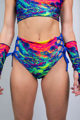 Model showcasing Freedom Rave Wear's high-waisted rave shorts with a vivid dinosaur sunset print, blue lace-up sides, and matching gloves.