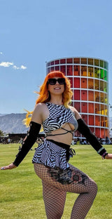 A woman wearing a black and white geometric skirt that ties on the side with a matching crop top. She is posing at a music festival.