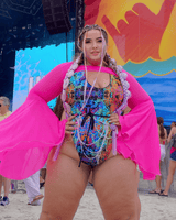 rave girl in colorful trippy rainbow rave outfit bodysuit with pink bell sleeves on a beach