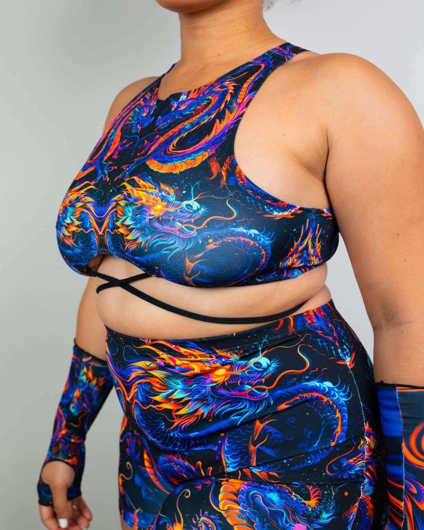 Model wearing ShadowFlame Teaser Top, a colorful cropped rave outfit with dragon design and criss-cross straps.