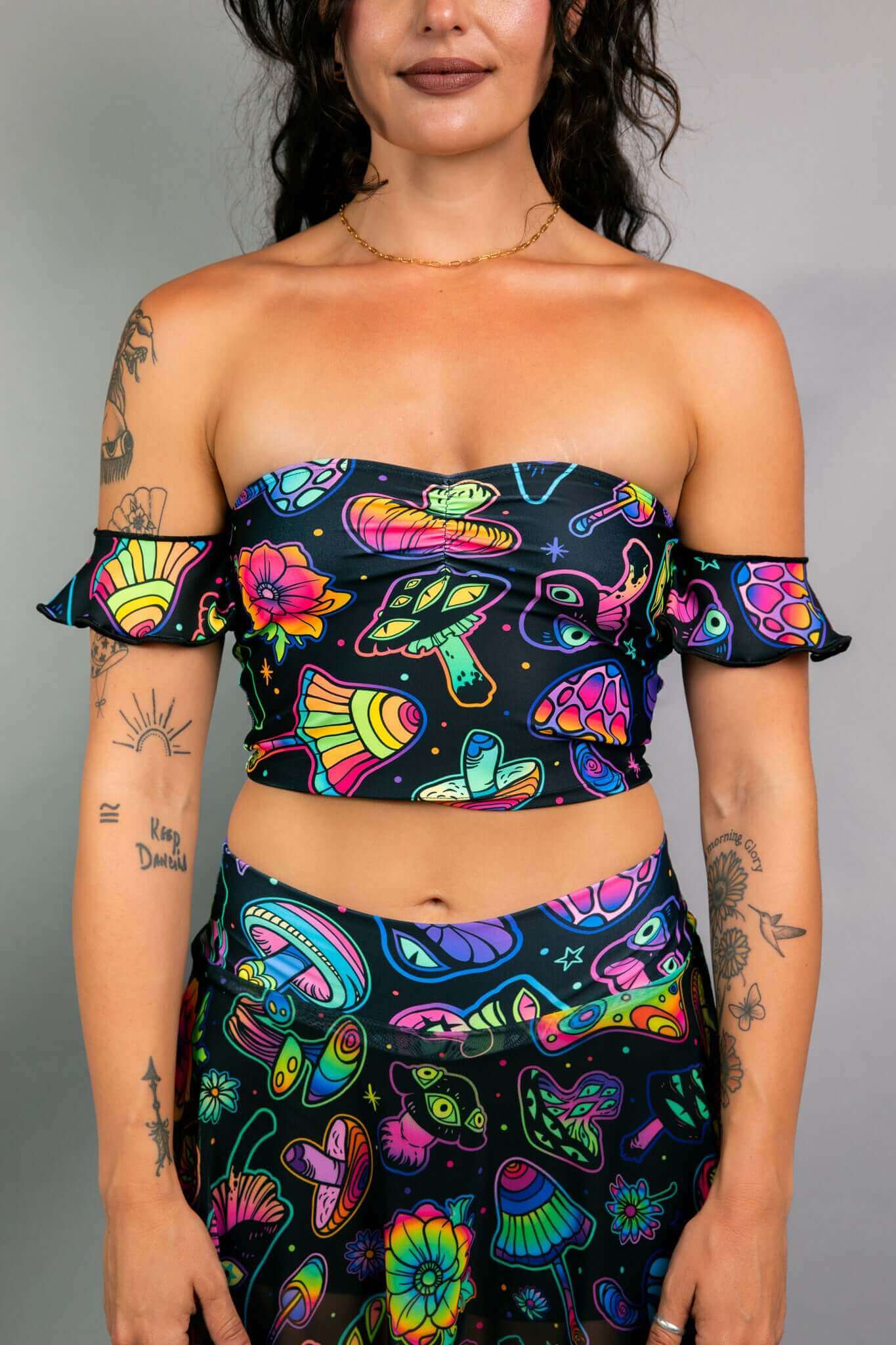 Model wearing a Freedom Rave Wear off-the-shoulder crop top with ruffle sleeves and matching high-waisted skirt in a psychedelic mushroom and flower print.