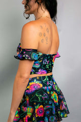 Side view of a model wearing a Freedom Rave Wear off-the-shoulder crop top and skater skirt set. The outfit features a vibrant psychedelic mushroom and floral print.