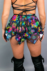 Rear view of a model in a Freedom Rave Wear psychedelic skater skirt with colorful mushroom and flower prints, featuring an asymmetrical hem.