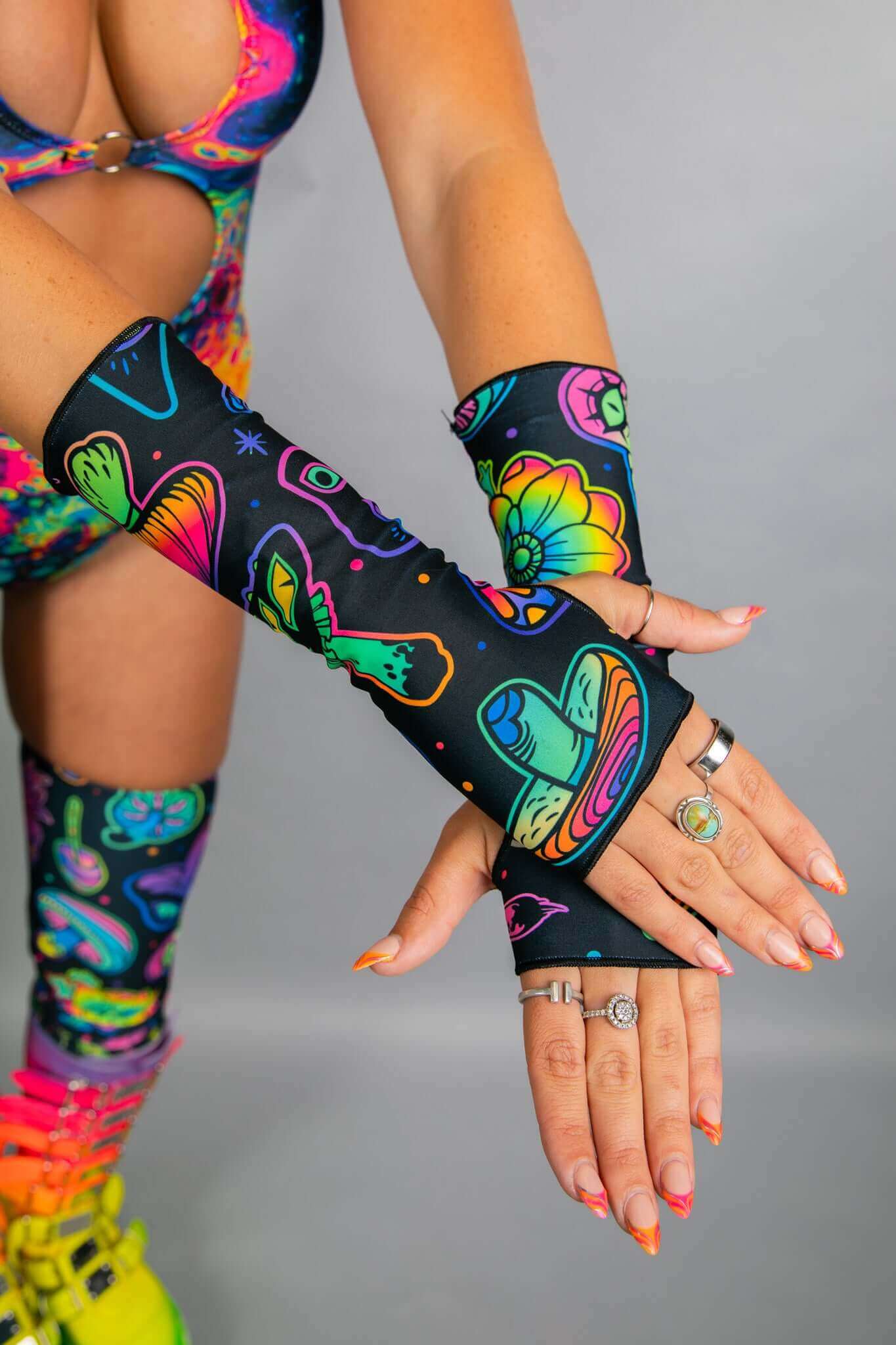 Close-up of model’s hands wearing Freedom Rave Wear fingerless gloves featuring neon mushroom and floral patterns, with matching bodysuit visible.