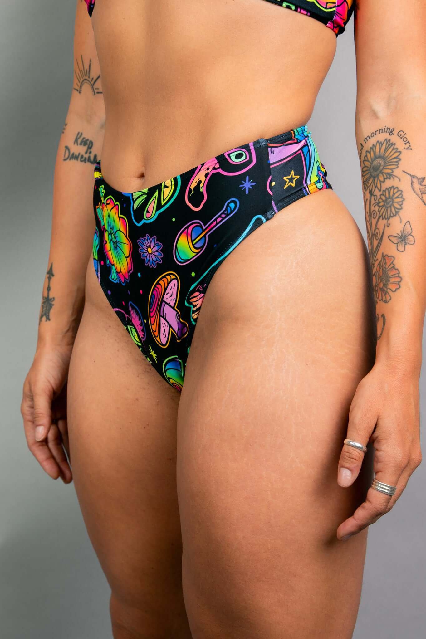  Side view of Freedom Rave Wear high-waisted rave bottoms featuring psychedelic mushrooms and flowers in vibrant neon colors on a black base.