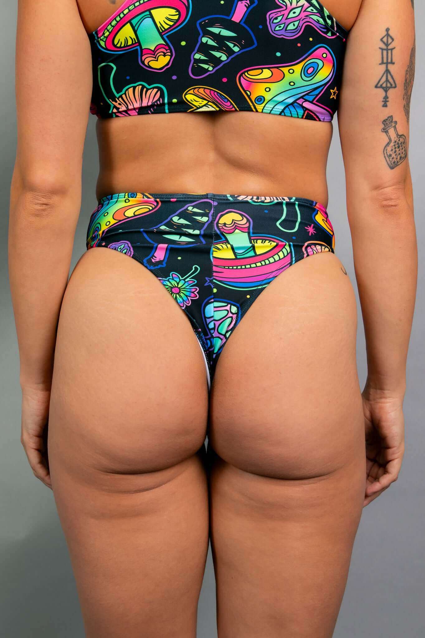 Back view of Freedom Rave Wear high-waisted rave bottoms, showcasing vibrant psychedelic mushroom and floral designs on a black base.