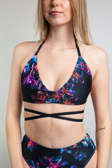 Freedom Rave Wear model in a supportive black Extra Mile bralette with vibrant neon floral patterns and multiple criss-cross straps.