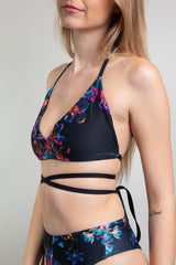 Freedom Rave Wear model in a supportive black Extra Mile bralette with vibrant neon floral patterns and multiple criss-cross straps.