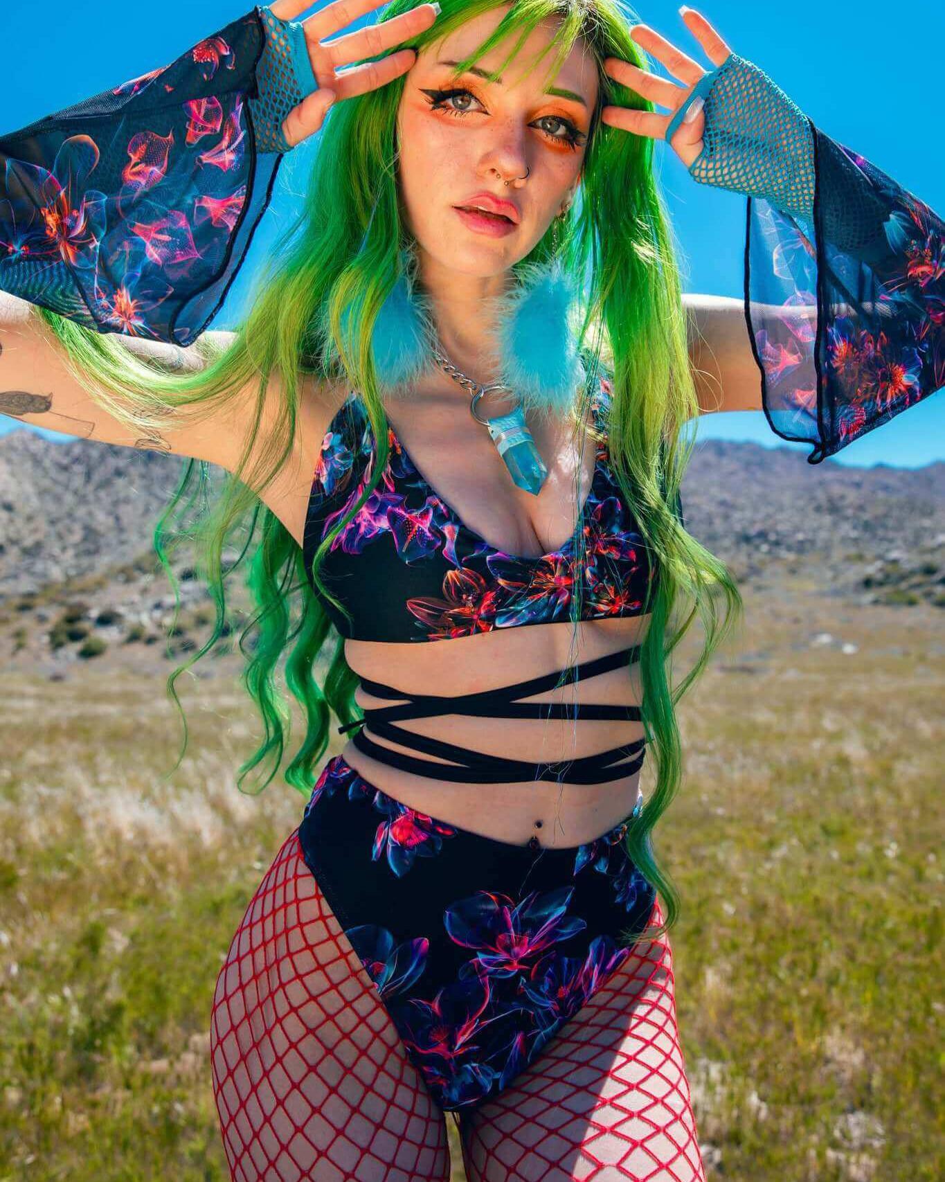 Model wearing Starflora mesh flare sleeves, floral rave outfit, green hair, outdoor setting with sunny skies.