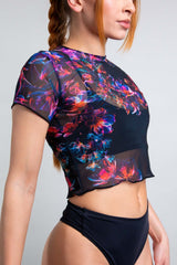 Freedom Rave Wear model poses in a stylish sheer black rave top featuring a vivid neon floral pattern, designed for a chic look.