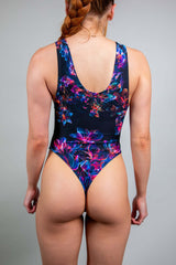 Rear view of a model in a Freedom Rave Wear sleeveless floral rave bodysuit, featuring a low scoop back and vibrant print detailing.