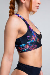 Profile view of a model in a Freedom Rave Wear two-piece floral swimsuit, showing the side mesh panel and detailed vibrant print.