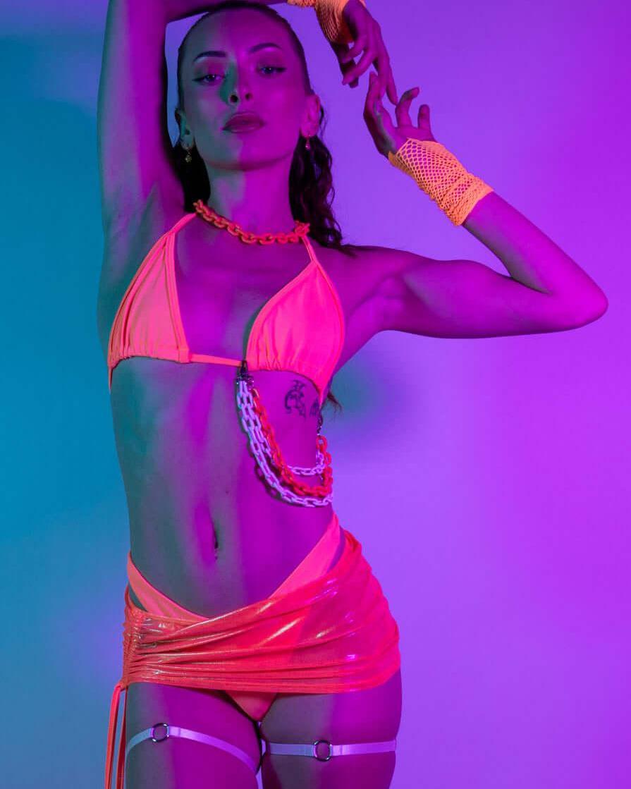 Model wearing Valencia Bikini Top in neon coral, styled for rave outfits with vibrant lighting and accessories.