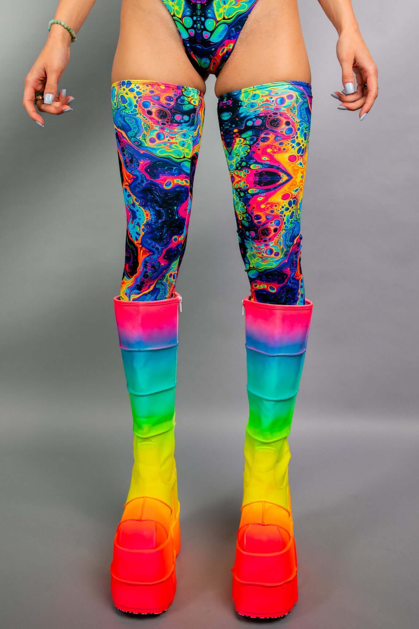 Close-up of Freedom Rave Wear's thigh-high leggings in a vibrant psychedelic pattern, paired with rainbow gradient platform boots.