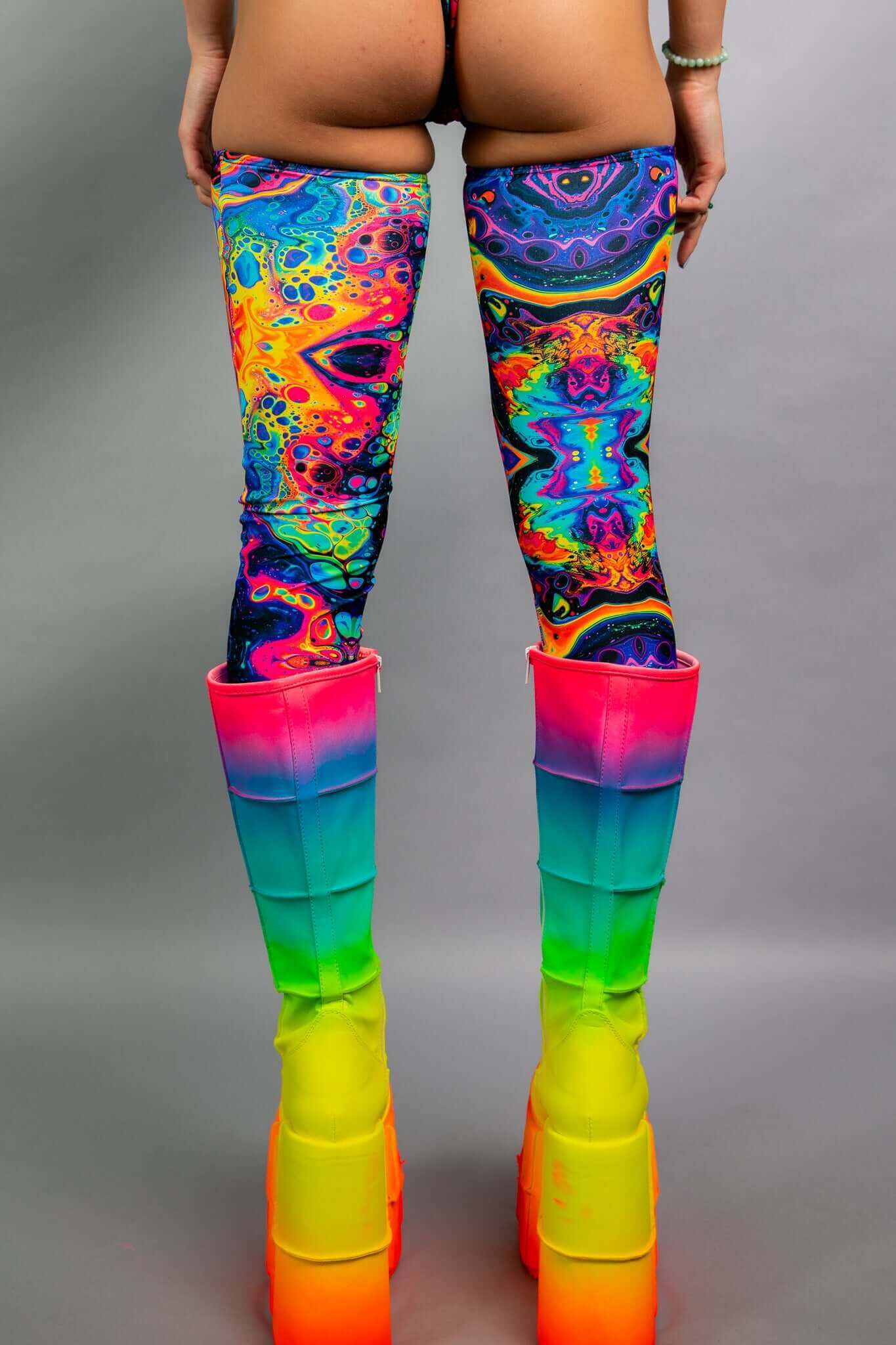 Back view of Freedom Rave Wear's psychedelic thigh-high leggings, showcasing vibrant, swirling patterns paired with bold rainbow platform boots for an eye-catching rave look.