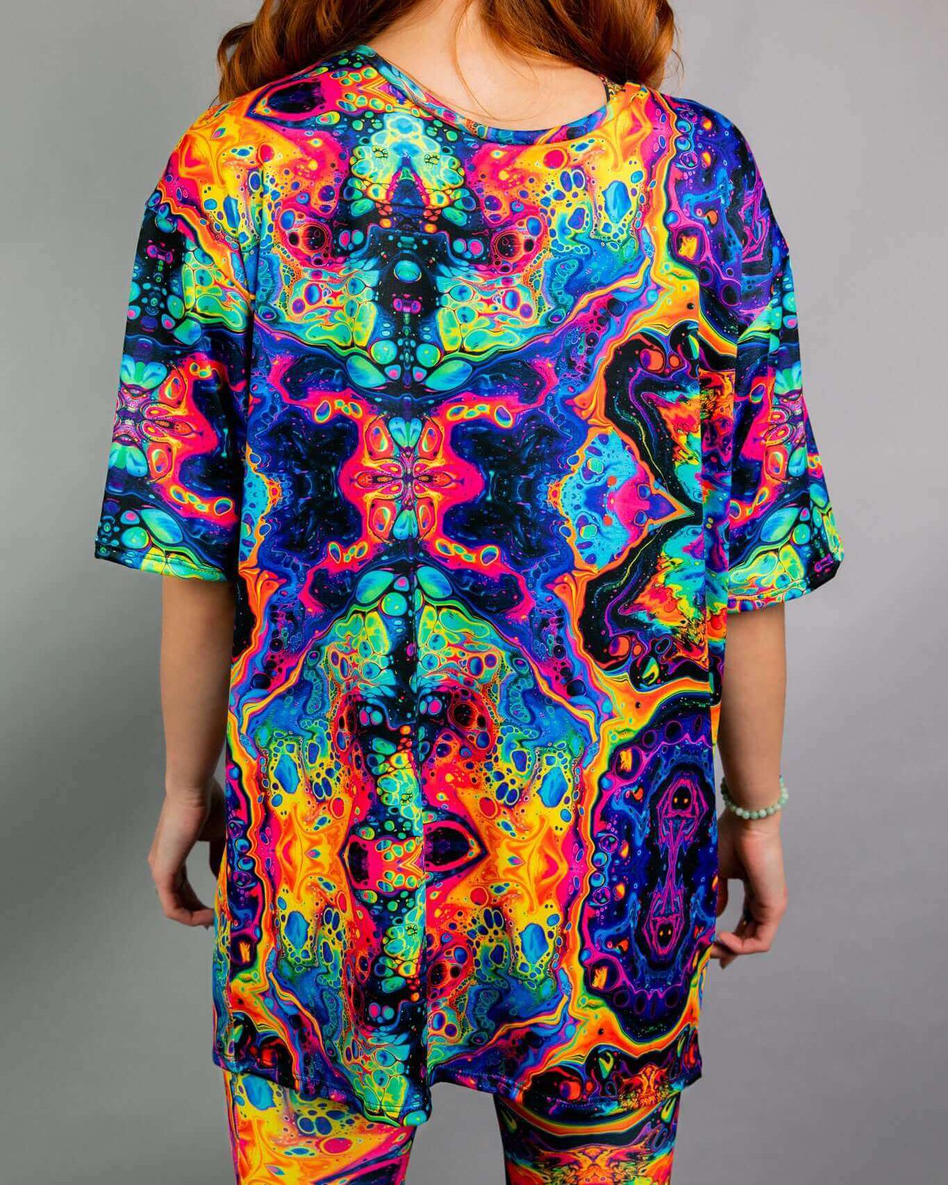 Back view of a woman in a vibrant, oversized rainbow rave tee, showcasing colorful trippy patterns and comfort.