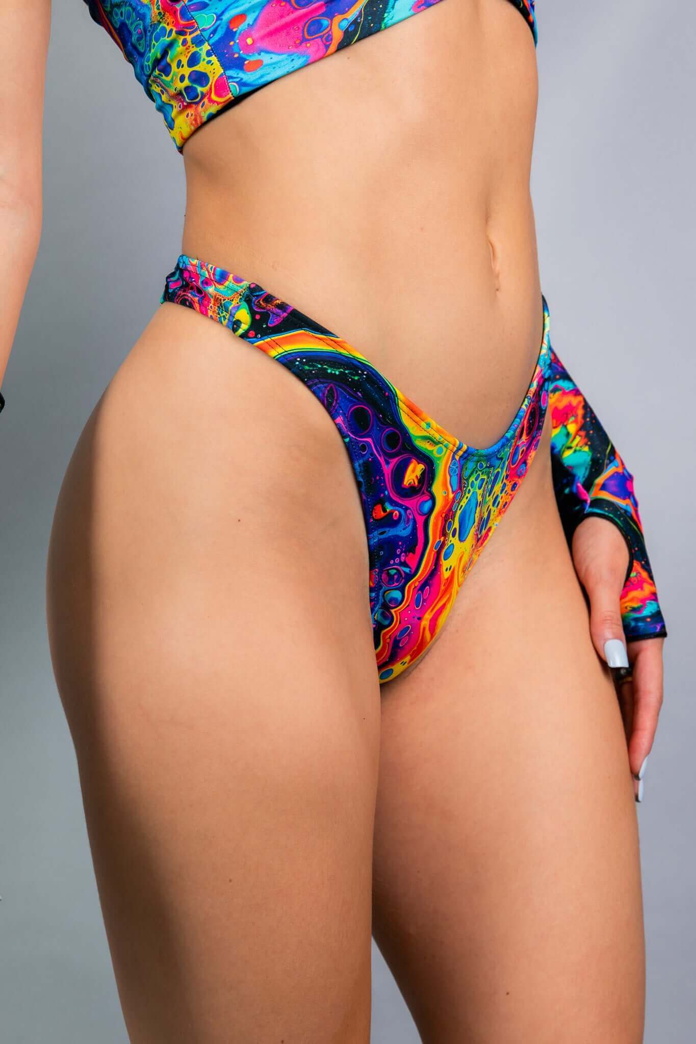 A close-up side view of a Freedom Rave Wear high-leg bikini bottom in a vibrant psychedelic swirl pattern, paired with matching arm sleeves.