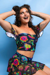 Shroomie Bardot top with colorful patterns, off-shoulder ruffles, perfect for rave outfits, modeled by a woman with curly hair.