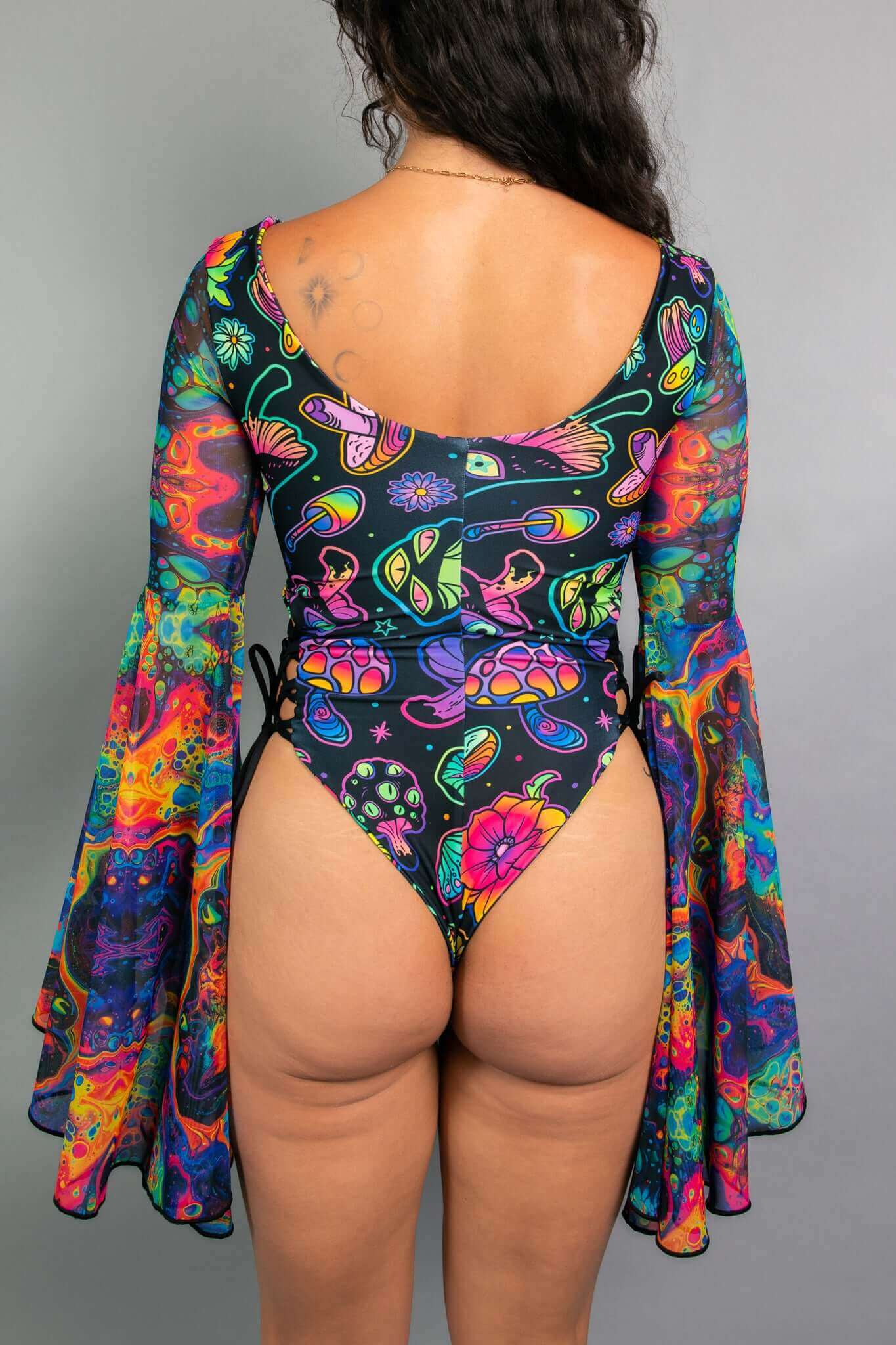 Back view of a model in a Freedom Rave Wear bodysuit, featuring a vibrant mushroom and floral print, deep scoop back, and flared bell sleeves.