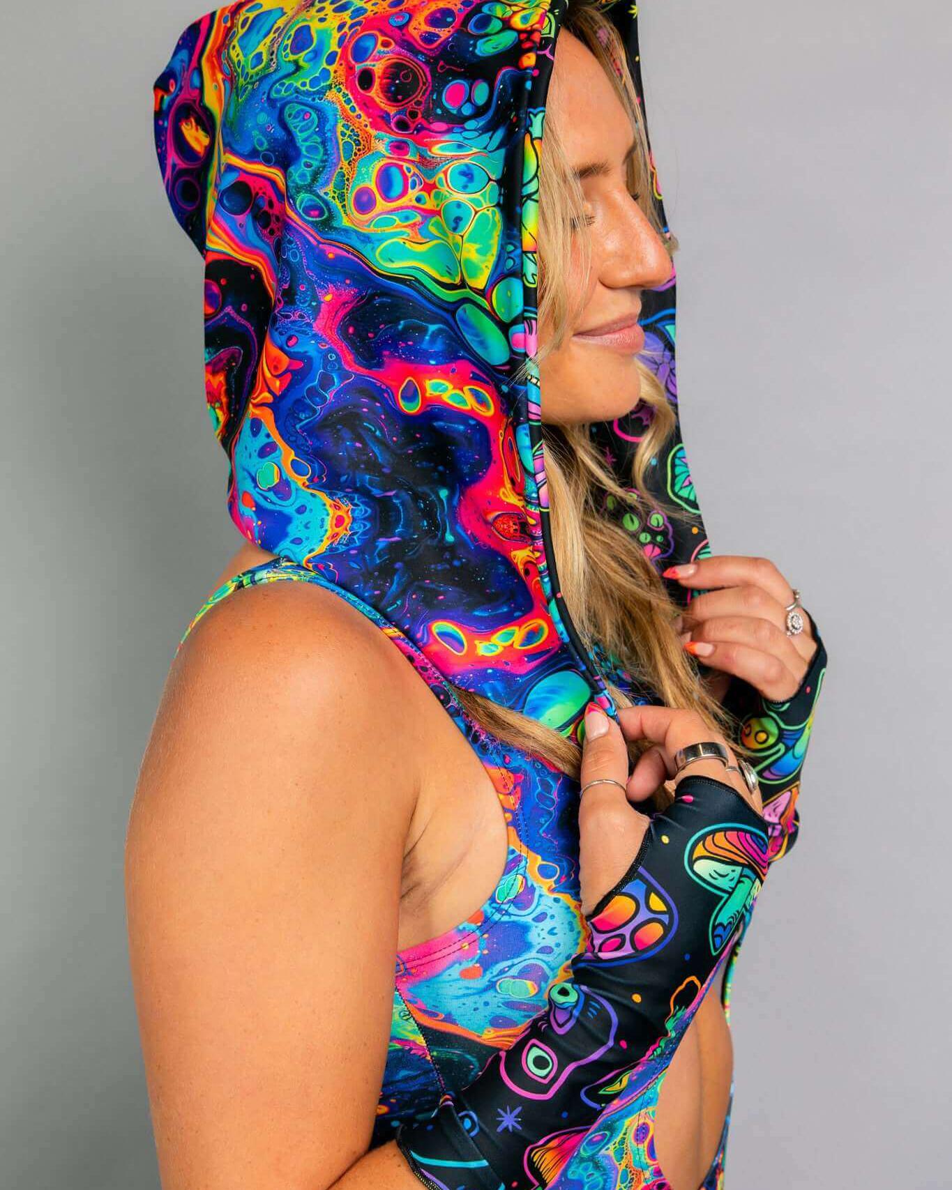 Vivid Shroomie! Assassin Hood in rainbow and mushroom print, worn by a model at a rave, showcasing vibrant festival style.