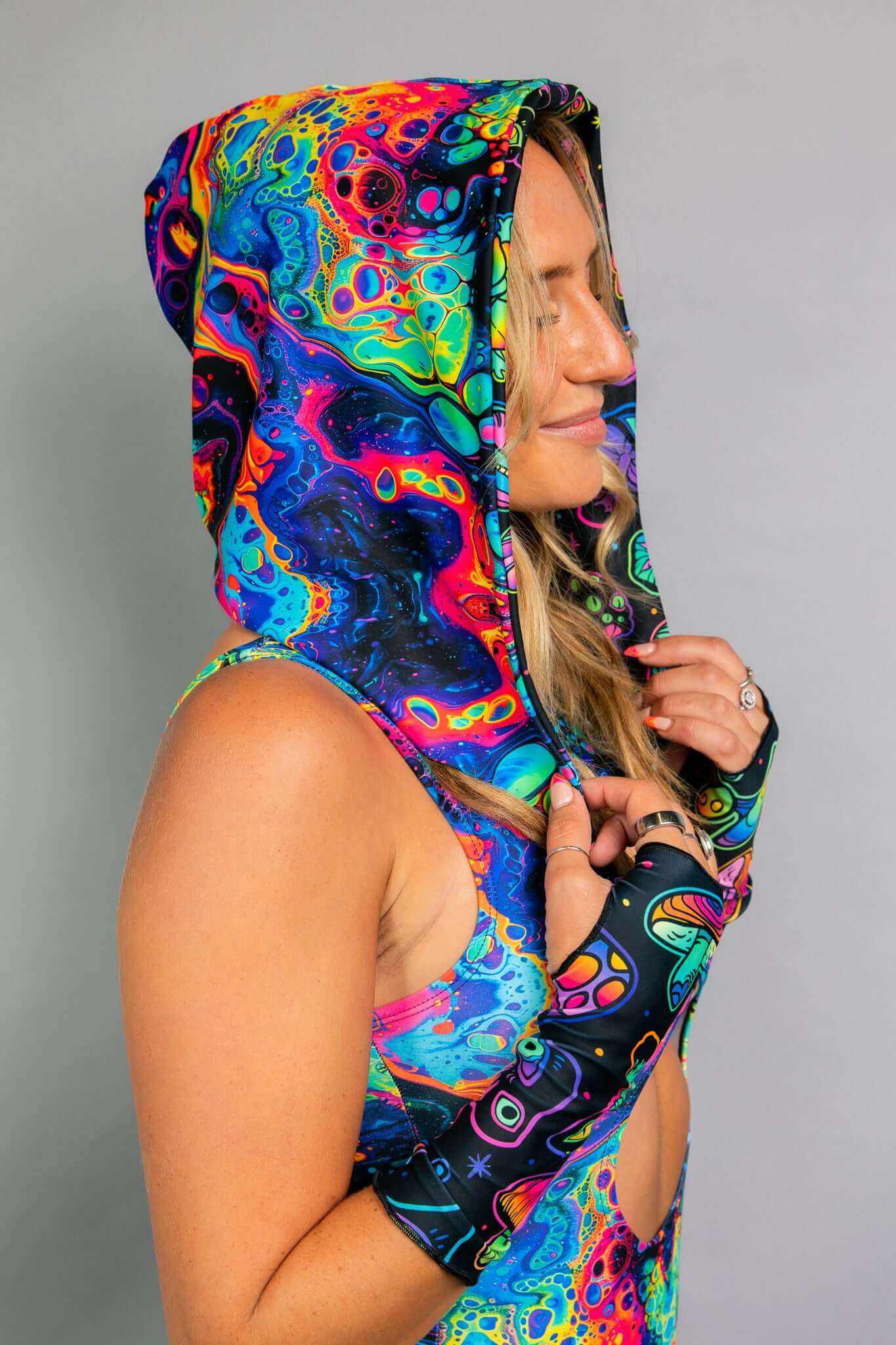 A side profile of a model wearing a Freedom Rave Wear hooded top with psychedelic swirl patterns, paired with matching fingerless gloves.