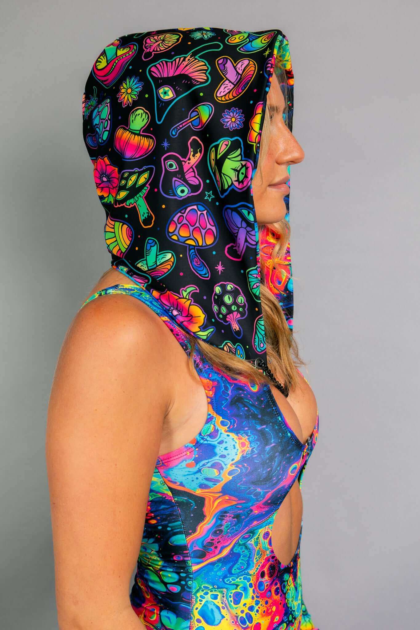 A side profile of a model wearing a Freedom Rave Wear hooded top featuring vibrant psychedelic mushroom patterns, paired with a matching bodysuit showcasing colorful abstract swirls.