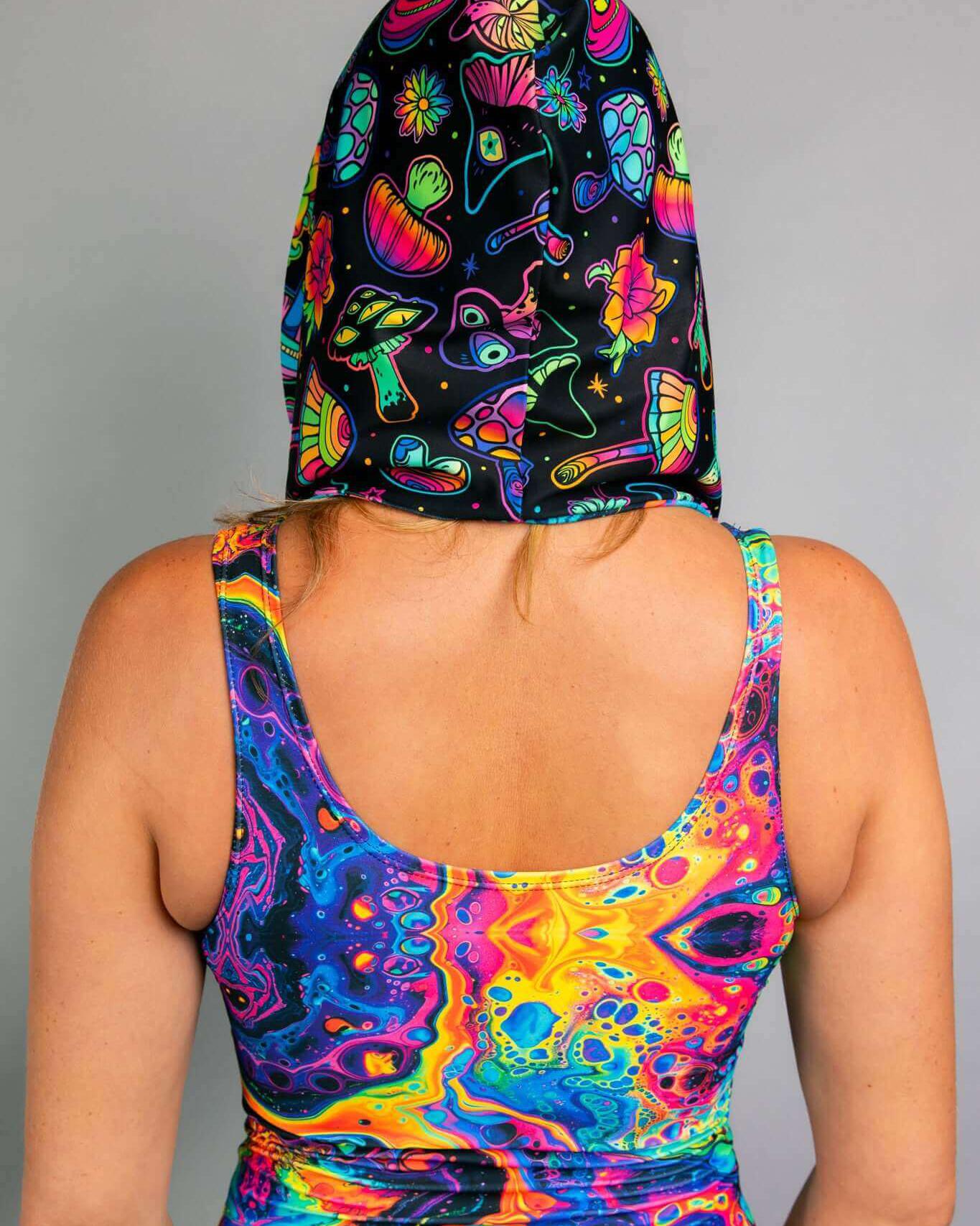 Colorful back view of a woman wearing the Vivid Shroomie! Assassin Hood with psychedelic rainbow prints, perfect for rave outfits.