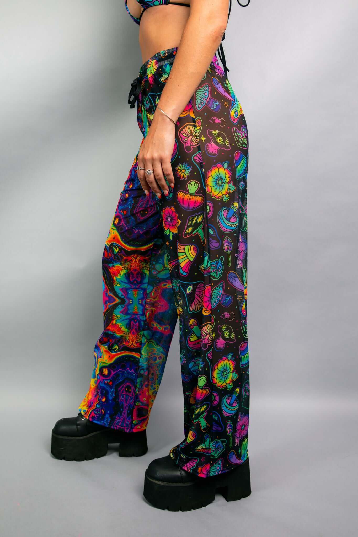 Side view of a model wearing Freedom Rave Wear pants with a vibrant mix of psychedelic patterns, including mushrooms and floral designs. Ideal for rave and festival fashion.