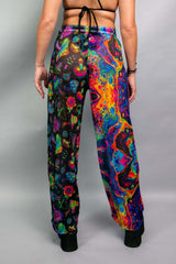 Back view of a model wearing Freedom Rave Wear pants with a vibrant mix of psychedelic patterns, including mushrooms and abstract designs. Perfect for rave and festival attire.