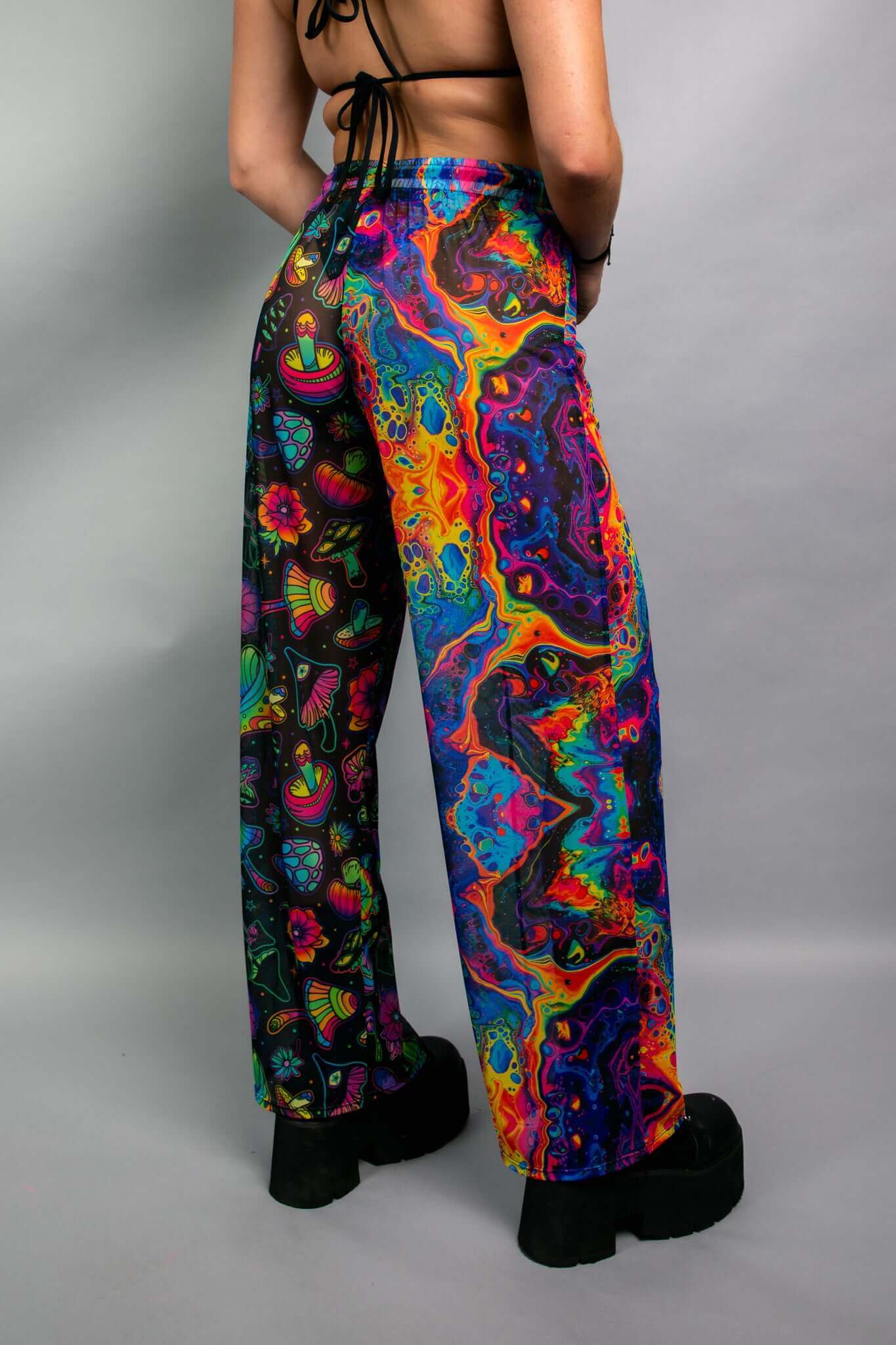 Side view of a model wearing Freedom Rave Wear pants with a vibrant mix of psychedelic patterns, including mushrooms and abstract designs. Ideal for rave and festival fashion.