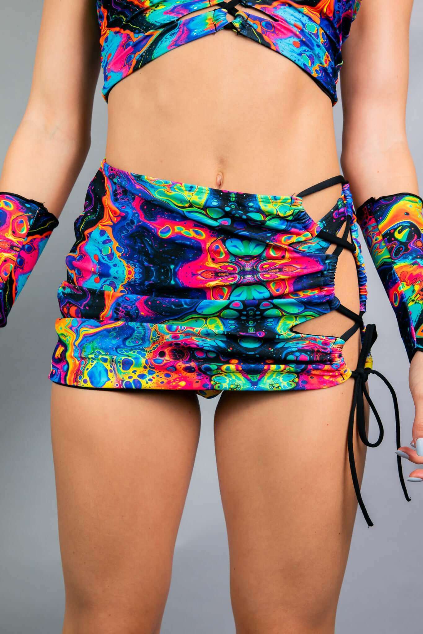 Freedom Rave Wear features a vibrant rave skirt with side cutouts and lace-up details, modeled by a person showcasing a psychedelic neon pattern. Perfect for standout festival looks.