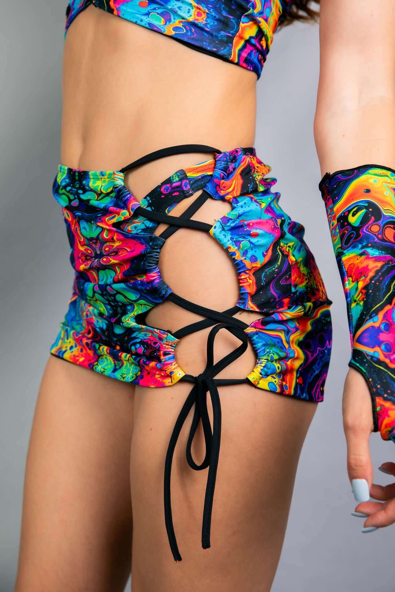 Model wearing a Freedom Rave Wear skirt with side cutouts and lace-up details, showcasing a psychedelic neon pattern. Perfect for rave fashion.