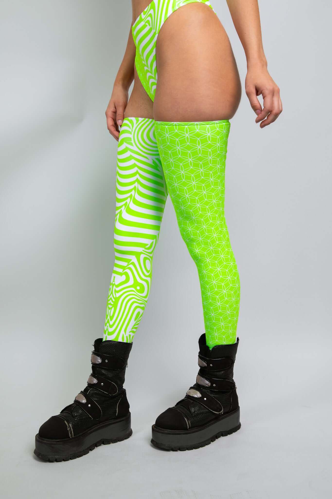 Side view of a woman in a Freedom Rave Wear outfit with green and white patterns, wearing thigh-high leggings and black boots.